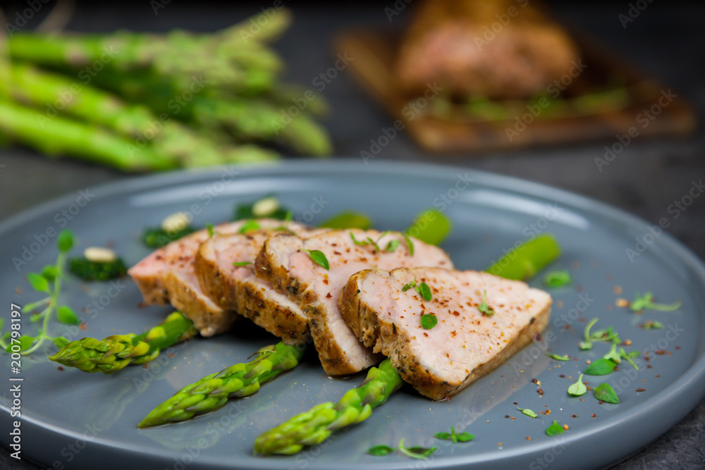 Slices of roasted pork tenderloin on asparagus with pesto from kale and thyme on the grey plate. Asparagus and all pork tenderloin on the background Slices of roasted pork tenderloin on asparagus with pesto from kale and thyme on the grey plate. Asparagus and all pork tenderloin on the background