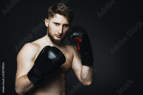 Blonde caucasian man staying on a black background with gloves in hands. © Strelciuc