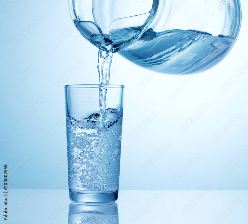 pouring water from pitcher into the glass on light blue background Stock  Photo