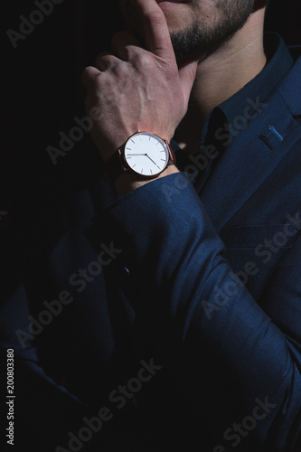 A dark portrait of a man dressed in an expensive suit, adjusting an elegant wrist watch