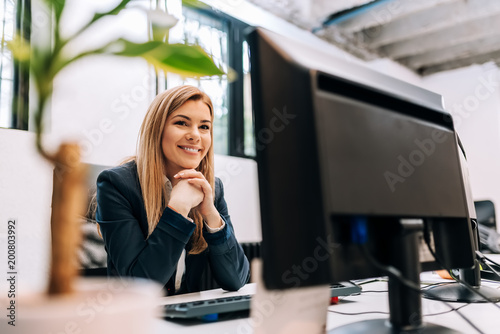 Sucessful smiling businesswoman sitting at the office in front of a computer.