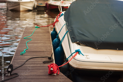 a modern motor boat windshield and bow deck covered in a blue canvas rain cover, with a weathered wood dock and blurry port in background