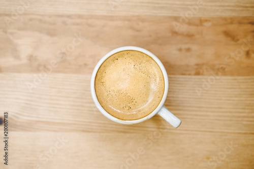 Top view of white coffee cup filled with fresh hot espresso on wooden background