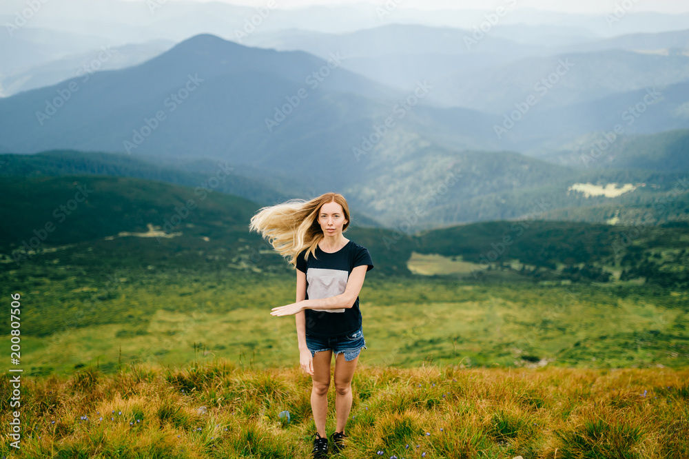 Young beautiful odd blonde girl mood portrait.  Unusual female person with flying hair in motion. Traveler cute babe strange gestures. Tourist woman at top of mountain enjoying freedom and relaxing.