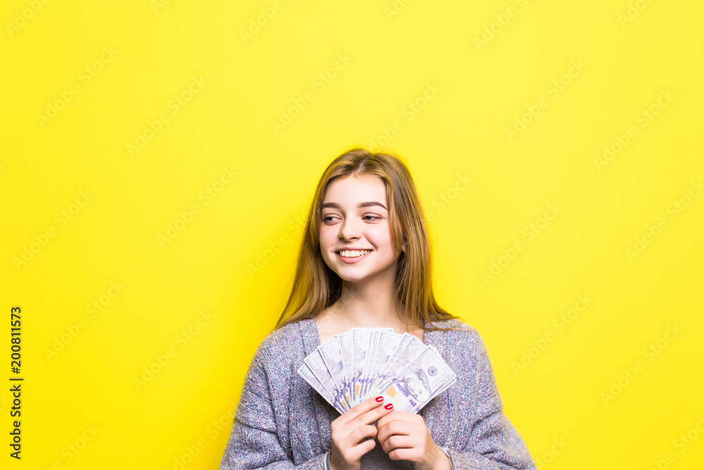Joyful teenage girl with dollars in her hands isolated on yellow background Joyful teenage girl with dollars in her hands isolated on yellow background