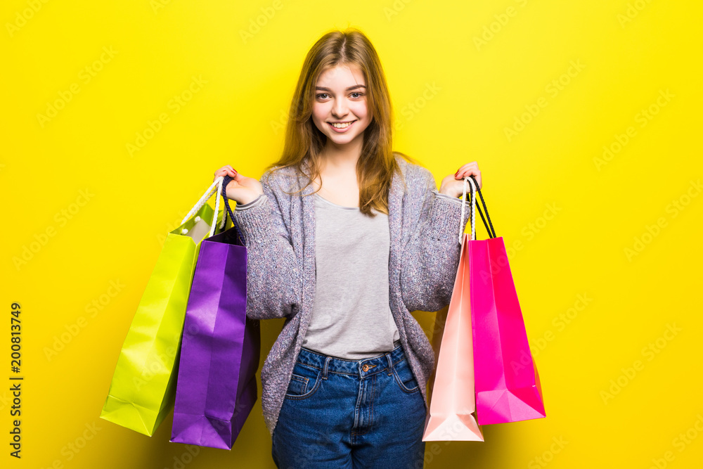 Portrait of young happy smiling teen girl with shopping bags, isolated over yellow background