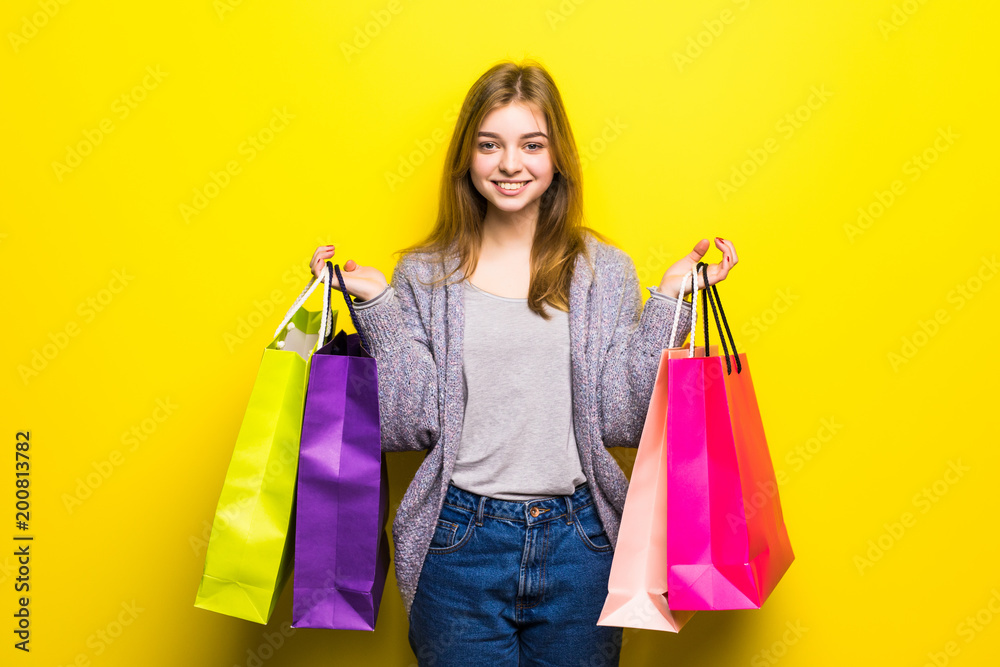 Happy teenage girl with shopping bags isolated on yellow background