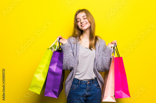 Pretty teenage girl with color shopping bags in studio against yellow background