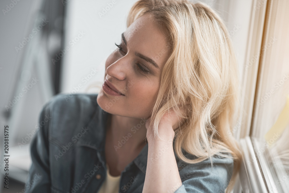 Portrait of young woman by the window staring aside. Her expression is thoughtful Portrait of young woman by the window staring aside. Her expression is thoughtful