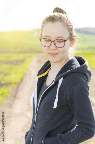A young Asian sporty girl wearing glasses and blue hoodie in a park. Preparing for sport or exercises.