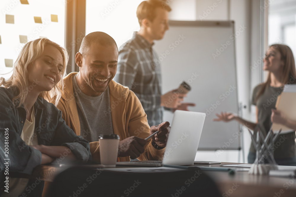 Man and woman watching interesting video at computer during coffee pause. Colleagues communicating on background