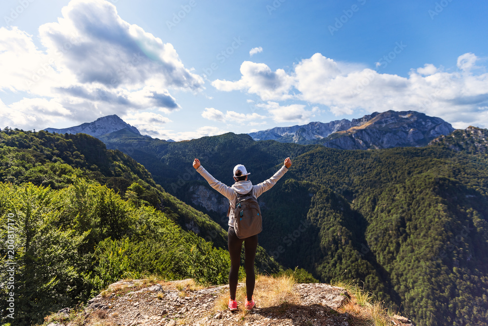 Female hiker with backpack raised her hands celebrating successful climb to top of mountain