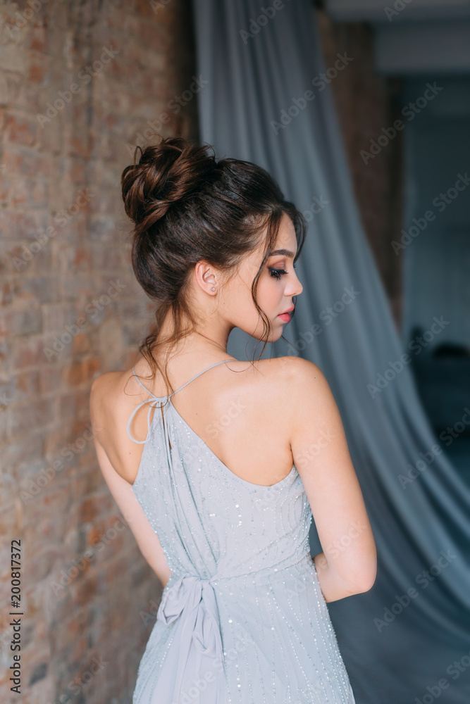 Young girl in a gray, evening dress posing on the camera. Bright evening  make-up with