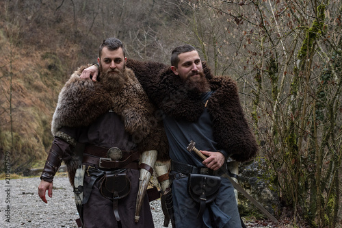 two Viking warriors walk hugged in the forest