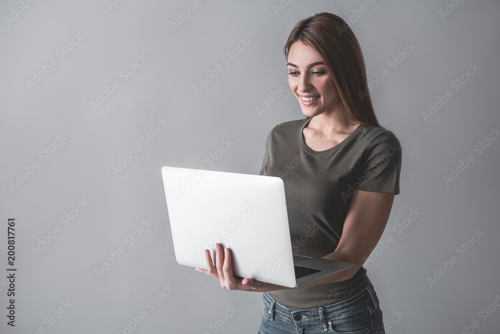 Waist up portrait of happy woman standing with laptop in hand. She is looking at gadget with joy. Isolated on background Waist up portrait of happy woman standing with laptop in hand. She is looking at gadget with joy. Isolated on background