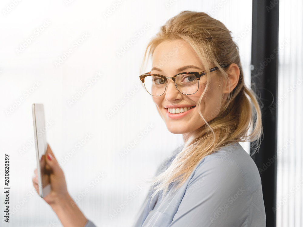 Portrait of confident blond businesswoman using portable computer and smiling. She is looking at camera with joy