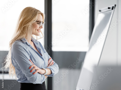 Side view of creative young woman looking at business plan on flipchart with confidence. She is standing in office and smiling