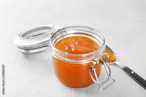 Jar and spoon with sweet jam on light background