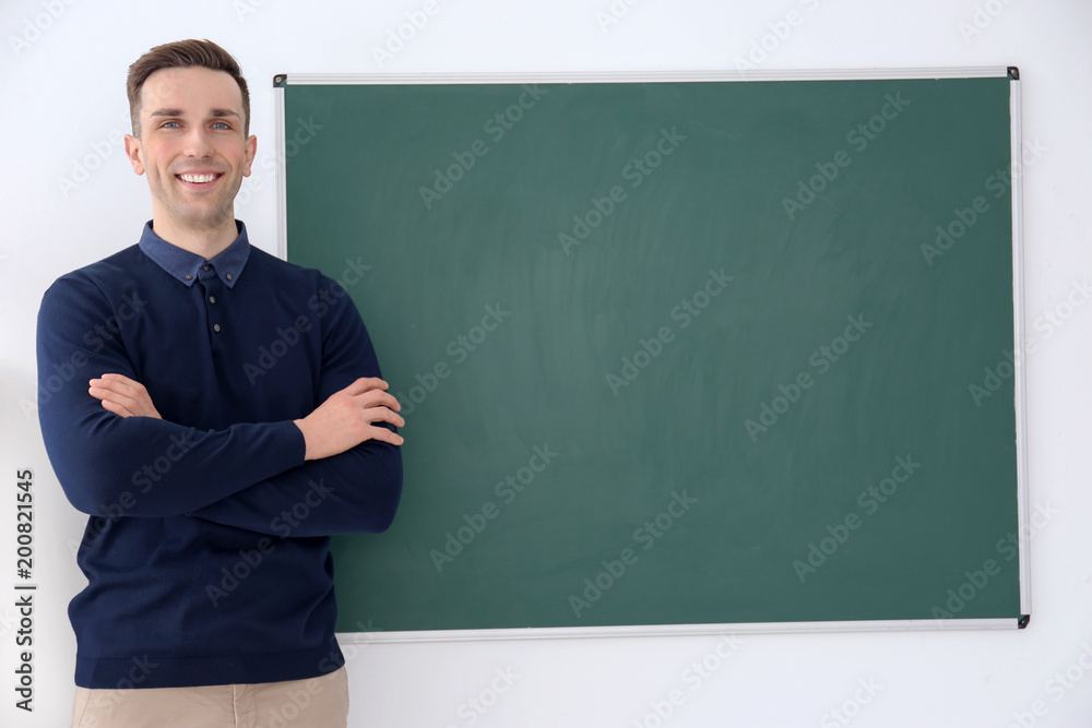 Young male teacher standing near blackboard on white background