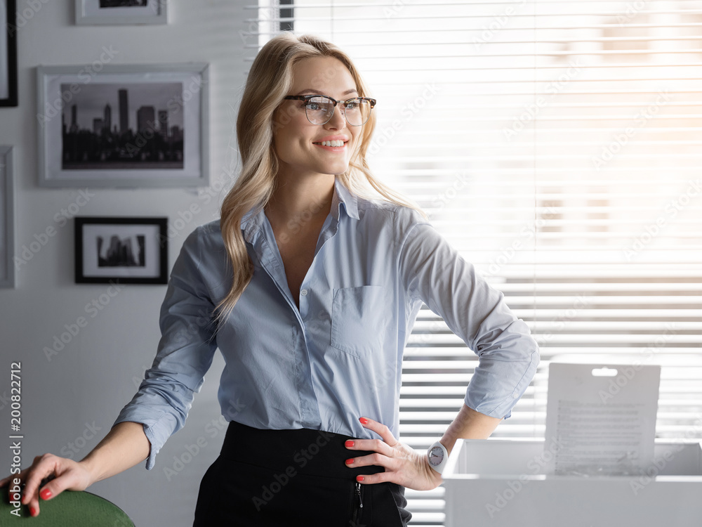 Portrait of confident young businesswoman standing in her office with arm akimbo. She is looking aside and smiling. Successful career concept Portrait of confident young businesswoman standing in her office with arm akimbo. She is looking aside and smiling. Successful career concept