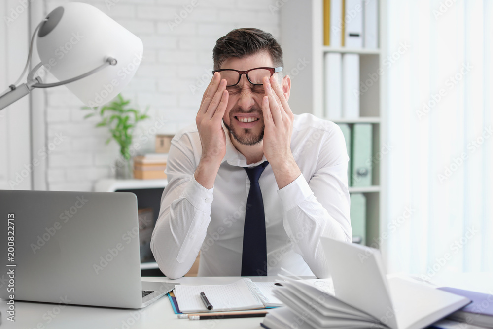 Man suffering from headache while sitting at table in office Man suffering from headache while sitting at table in office