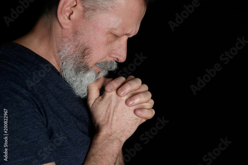 Religious senior man praying on black background