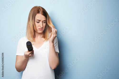 Young woman with hair loss problem on color background