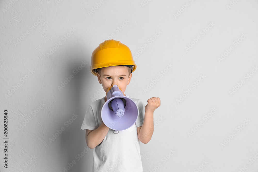 Adorable little boy in hardhat with megaphone on light background