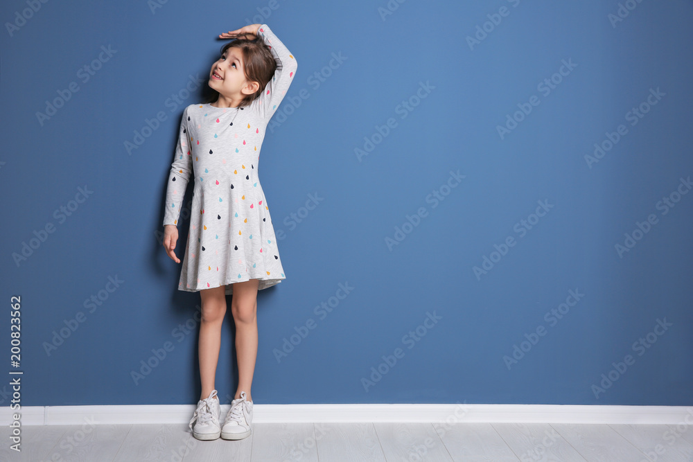 Little girl measuring her height near color wall - obrazy, fototapety, plakaty 