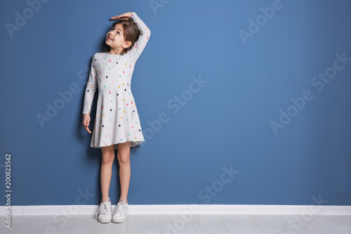 Little girl measuring her height near color wall