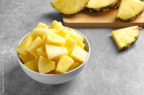 Bowl with fresh pineapple slices on grey background © New Africa