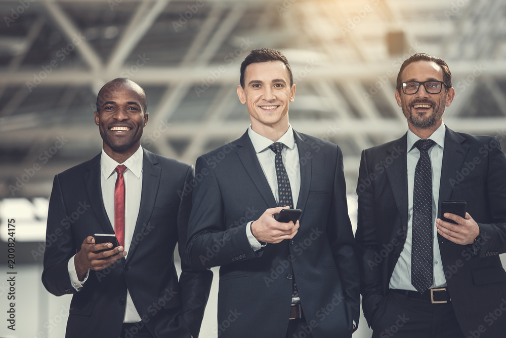 Portrait of satisfied businessmen working with cellphones while looking at camera. Happy partners sending messages concept Portrait of satisfied businessmen working with cellphones while looking at camera. Happy partners sending messages concept