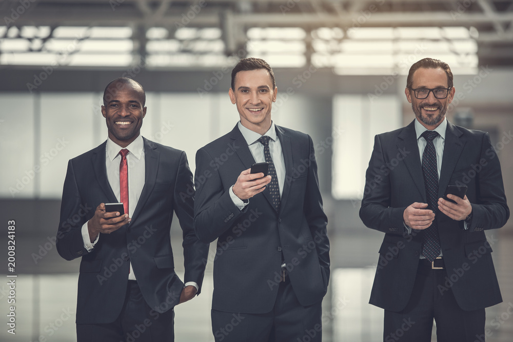 Portrait of beaming young male workers typing in mobiles. Glad colleagues using gadgets concept Portrait of beaming young male workers typing in mobiles. Glad colleagues using gadgets concept