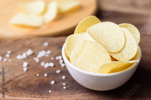 Potato chips in a bowl and salt on wooden background