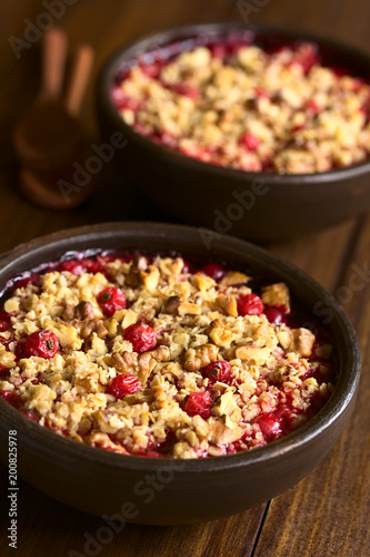 Redcurrant crumble or crisp with oatmeal and walnut on top baked in rustic bowl, photographed on dark wood with natural light (Selective Focus, Focus one third into the image)