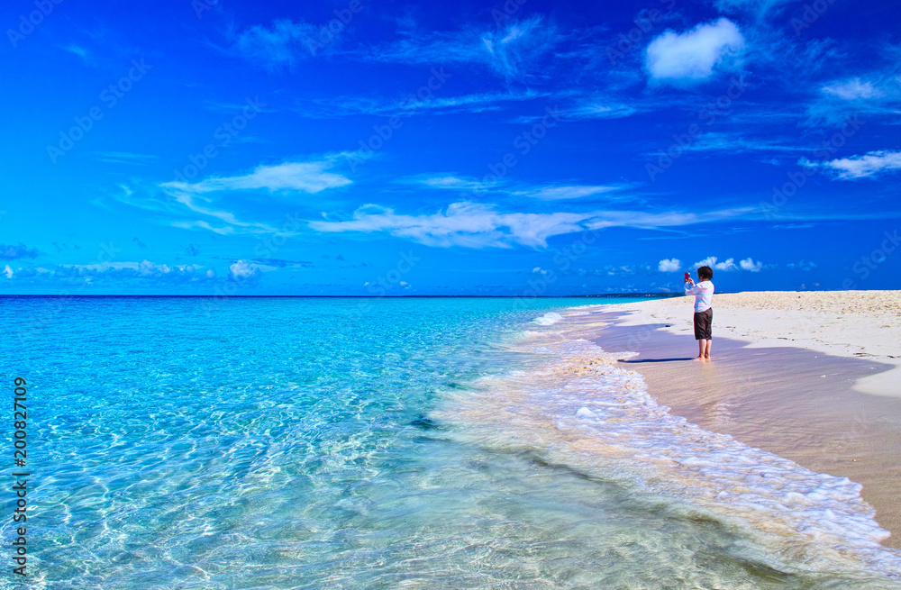 真夏の宮古島。与那覇前浜ビーチの風景とスマホで写真撮影をする女性
