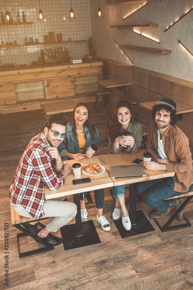 Naklejka premium Friendly talk. Top view of joyful young men and women relaxing in cafe together. They are looking at camera and smiling
