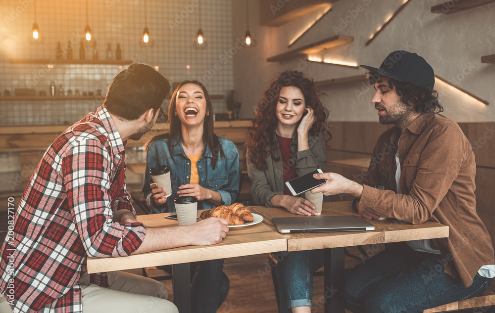 Cheerful young man and woman are dating in cafeteria and laughing. Their friends are sitting near them and talking, Entertainment concept