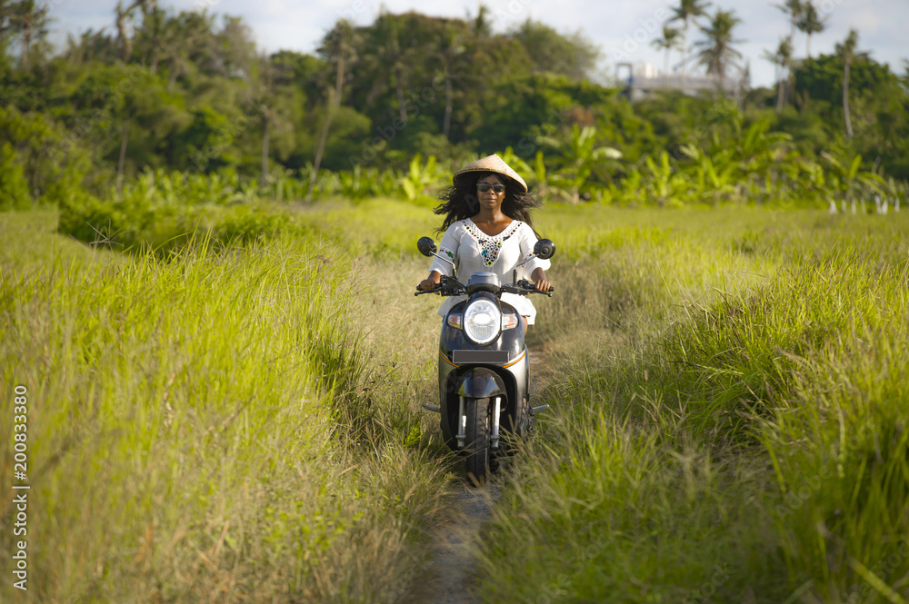 young beautiful tourist or nomad traveler black afro American woman riding motorbike in tropical field wearing traditional Asian hat smiling happy young beautiful tourist or nomad traveler black afro American woman riding motorbike in tropical field wearing traditional Asian hat smiling happy