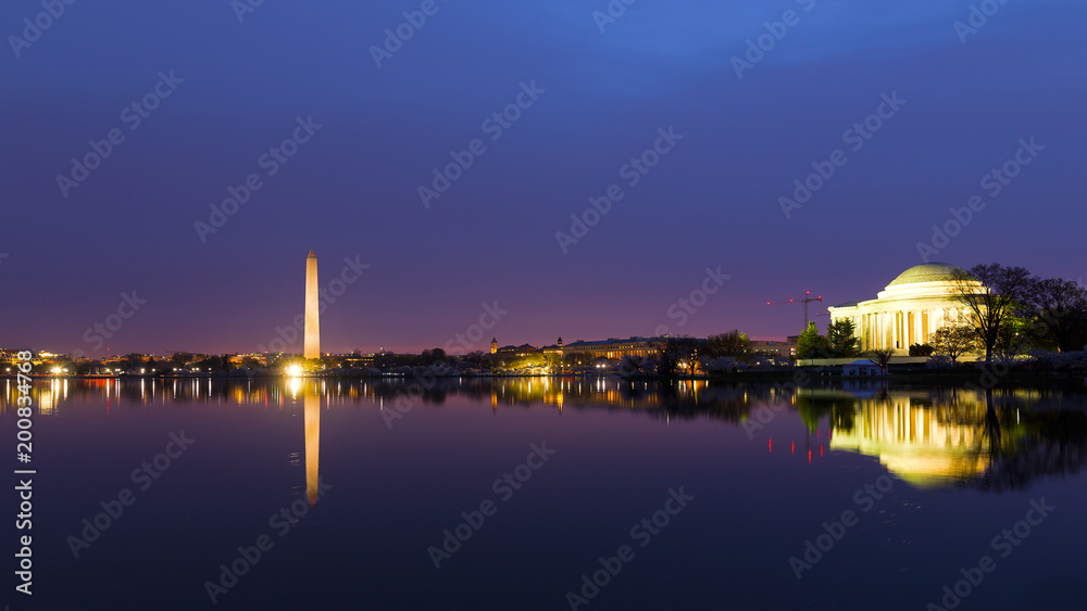 Washington DC panorama around Tidal Basin at sunrise during cherry blossom. City landmarks with reflection in dark waters at dawn.
