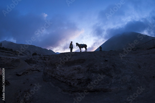 Men walking in Mount Bromo looking for tourist with his horse at sunset, Indonesia