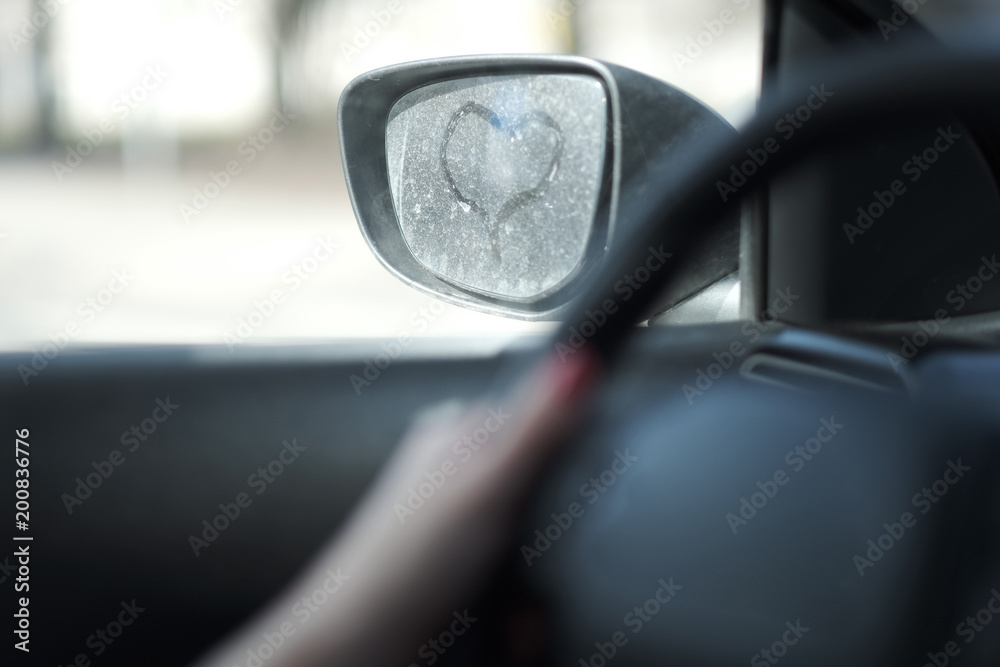 The symbolic image of the heart on a dusty car rearview mirror