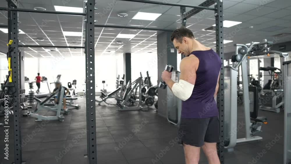 Muscular man with injured elbow training with dumbbell gym, recovery, strength Muscular man with injured elbow training with dumbbell gym, recovery, strength