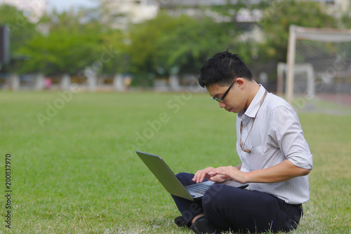 Relaxed young Asian business man working with laptop on green grass.