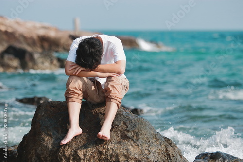 Lonely sad young Asian man feeling disappointed at the natural sea shore.