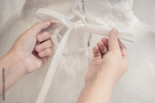 Bridesmaid helps the bride to wear  dress