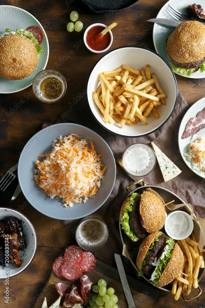 Outdoor table with burger, french fries, salad and snacks on wooden table with beer, top view. Outdoors food Concept