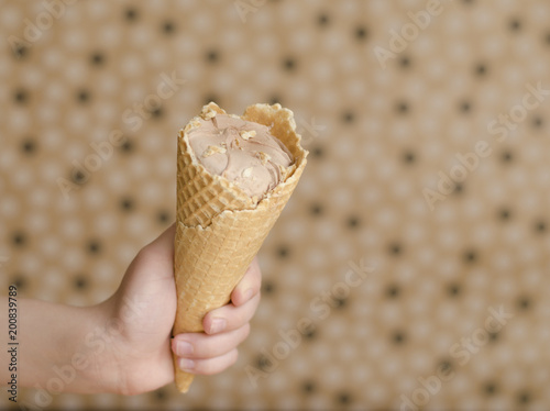 Chocolate ice cream in kid’ Hand on the beige background with space to the right