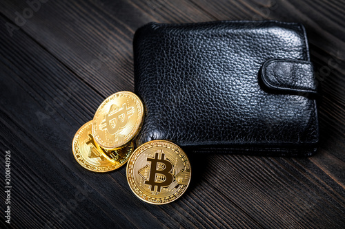 golden bitcoin and black purse on wood background