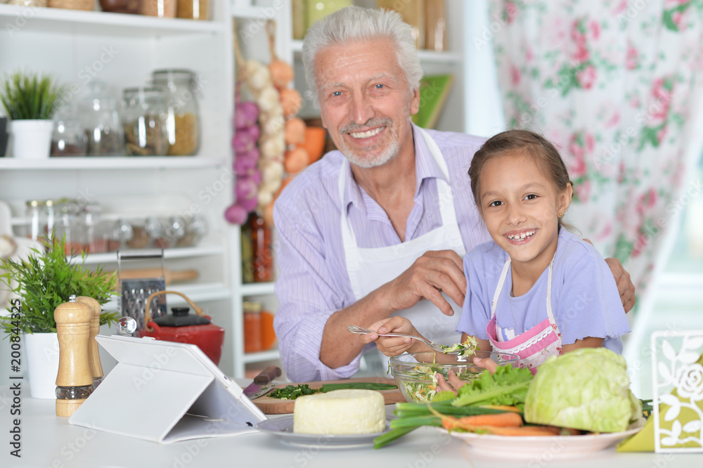 Senior man with granddaughter preparing dinner Senior man with granddaughter preparing dinner
